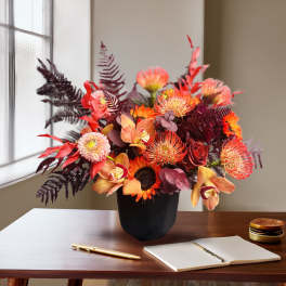 Orange and burgundy floral arrangement in a black vase on a desk