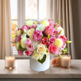 Pink and white flower arrangement in a white vase with candles