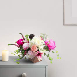 Pink and white floral arrangement in a square vase beside a candle