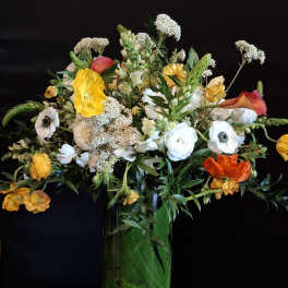 Tall mixed bouquet in a green glass vase with yellow, white, and orange flowers
