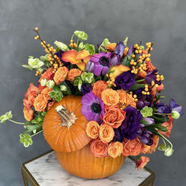Orange pumpkin centerpiece with purple and orange flowers