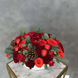 Red rose arrangement with pinecones and red ornaments in a white bowl