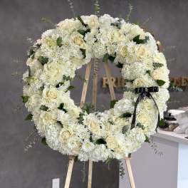 Large white floral wreath on a wooden easel with a black ribbon.