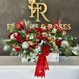 Red roses and holiday flowers in a white rectangular vase with ornaments