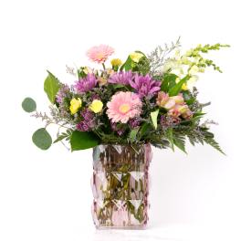Mixed bouquet of pink gerbera daisies, purple mums, and yellow roses in a pink textured glass vase