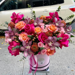 Pink and peach roses with purple orchids in a pink hatbox