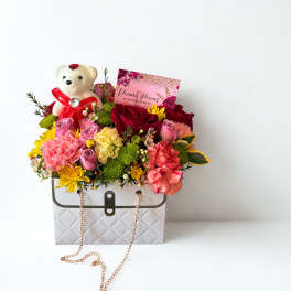 Flower arrangement in a white handbag box with a teddy bear