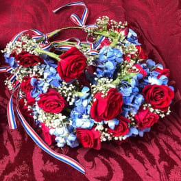 Heart-shaped floral wreath with red roses and blue flowers on a red fabric background