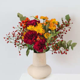 Bright mixed bouquet in a beige vase with red berries