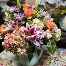 Mixed bouquet of roses, lilies, hydrangea, and daisies in a pale vase