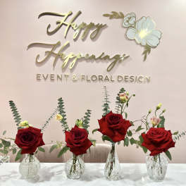 Four red rose arrangements in clear glass vases on a table