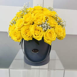 Yellow roses arranged in a black hatbox with white filler flowers