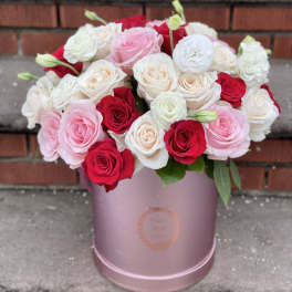 Pink, red, and white roses arranged in a pink round box