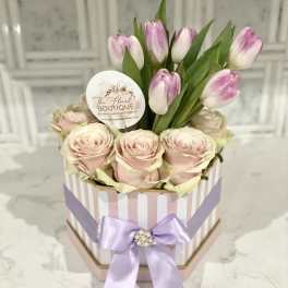 Pink roses and tulips arranged in a striped gift box with a lavender ribbon.