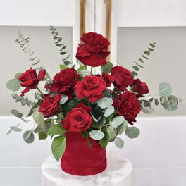 Red roses arranged in a red cylindrical vase with eucalyptus accents