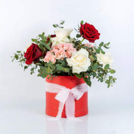 Red and white roses with pink carnations in a red box tied with a white ribbon