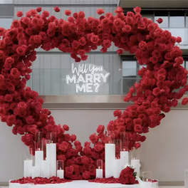 Large heart-shaped red rose display with candles and a "Will you marry me?" sign