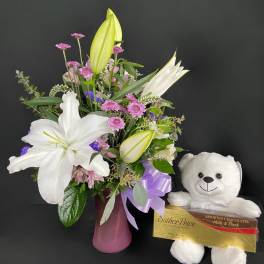 Bouquet of white lilies and pink flowers in a vase with a teddy bear and chocolates