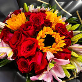 Bouquet of red roses, yellow sunflowers, and pink lilies wrapped in black paper