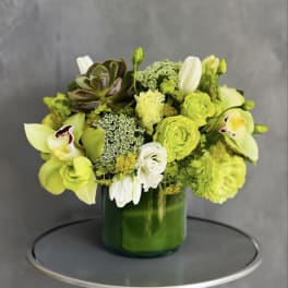 Green and white floral arrangement in a green glass vase