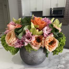 Mixed pink and peach flowers arranged in a gray vase