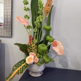 Tall tropical floral arrangement with pink anthuriums and green chrysanthemums in a gray vase