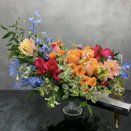 Colorful mixed bouquet in a clear glass vase with blue flowers and roses