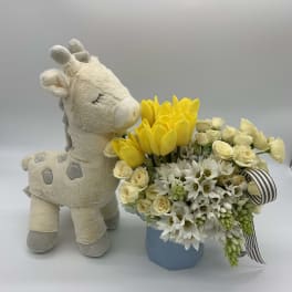 Plush giraffe beside a yellow and white flower arrangement in a blue box
