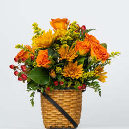 Orange roses and yellow mums in a woven basket with red berries