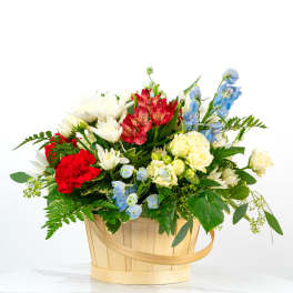 Red, white, yellow, and blue mixed flower basket arrangement in a light wood handled basket