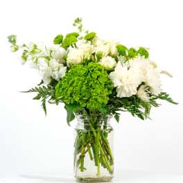 White and green mixed flower arrangement in a clear glass jar vase