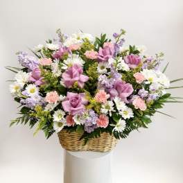 Basket arrangement of pink roses, daisies, carnations, and lavender flowers