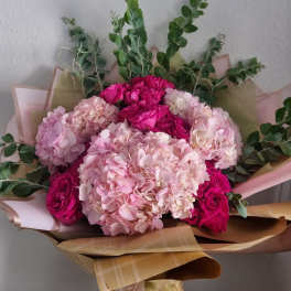 Bouquet of pink hydrangeas and magenta roses wrapped in tan paper