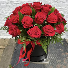 Red roses arranged in a black hatbox with a red ribbon