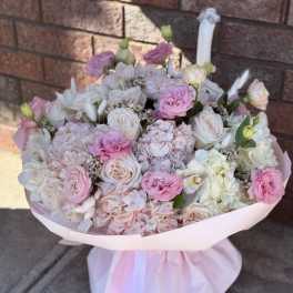 Pink and white bouquet of roses, hydrangeas, and carnations wrapped in pale pink paper