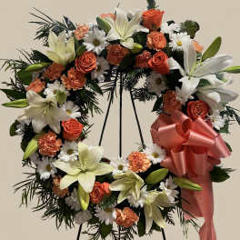 Heart-shaped floral wreath with lilies, roses, daisies, and a pink ribbon bow