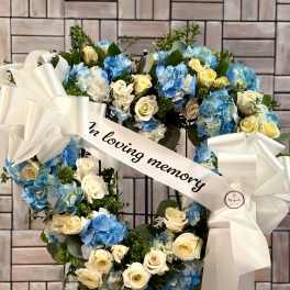 Heart-shaped wreath of blue hydrangeas and cream roses with white ribbon