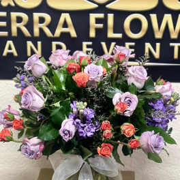 Lavender and coral roses in a round glass vase with a white ribbon