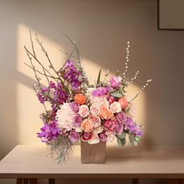 Mixed bouquet of pink, purple, and peach roses in a square vase