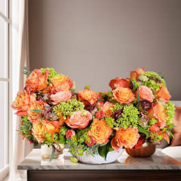 Three orange and peach rose arrangements in low containers on a table