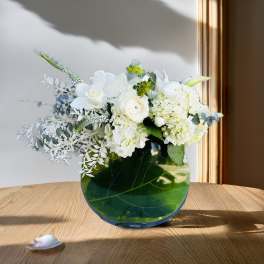 White floral arrangement in a round green glass vase