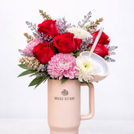 Bouquet of red roses and pink and white blooms in a blush tumbler vase