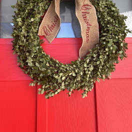 Green wreath with a burlap Christmas bow on a red door