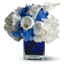 Compact arrangement of white calla lilies and blue and white hydrangeas in a cobalt blue glass cube vase