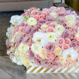 Large pastel bouquet of roses and white orchids in a striped box