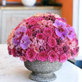 Pink rose arrangement with purple orchids in a gray pedestal vase