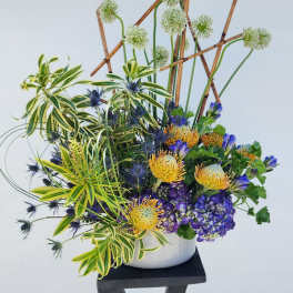 Tall floral arrangement in a white vase with purple, yellow, and blue blooms