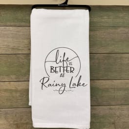White towel with "Life is Better at Rainy Lake" text on a hanger