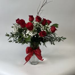 Red roses arranged in a glass vase with baby's breath and a red bow