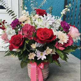 Mixed bouquet of red roses, pink blooms, and white flowers in a ribboned basket